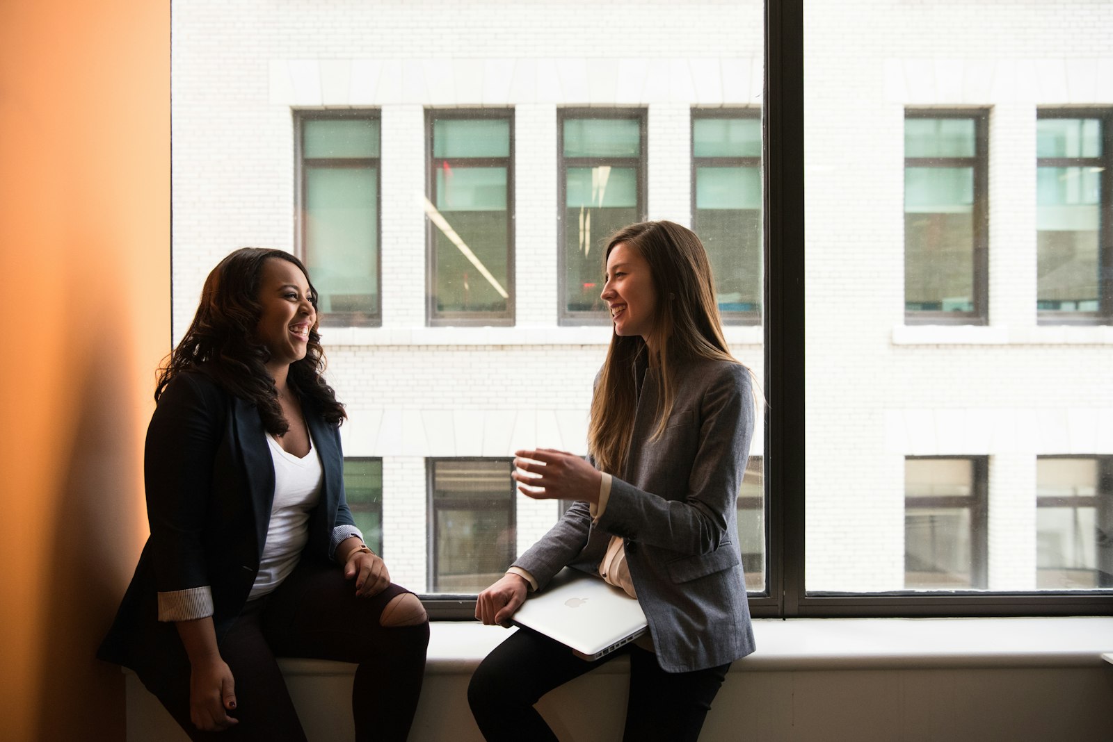 Two women in a relaxed, engaged mentoring conversation by a window